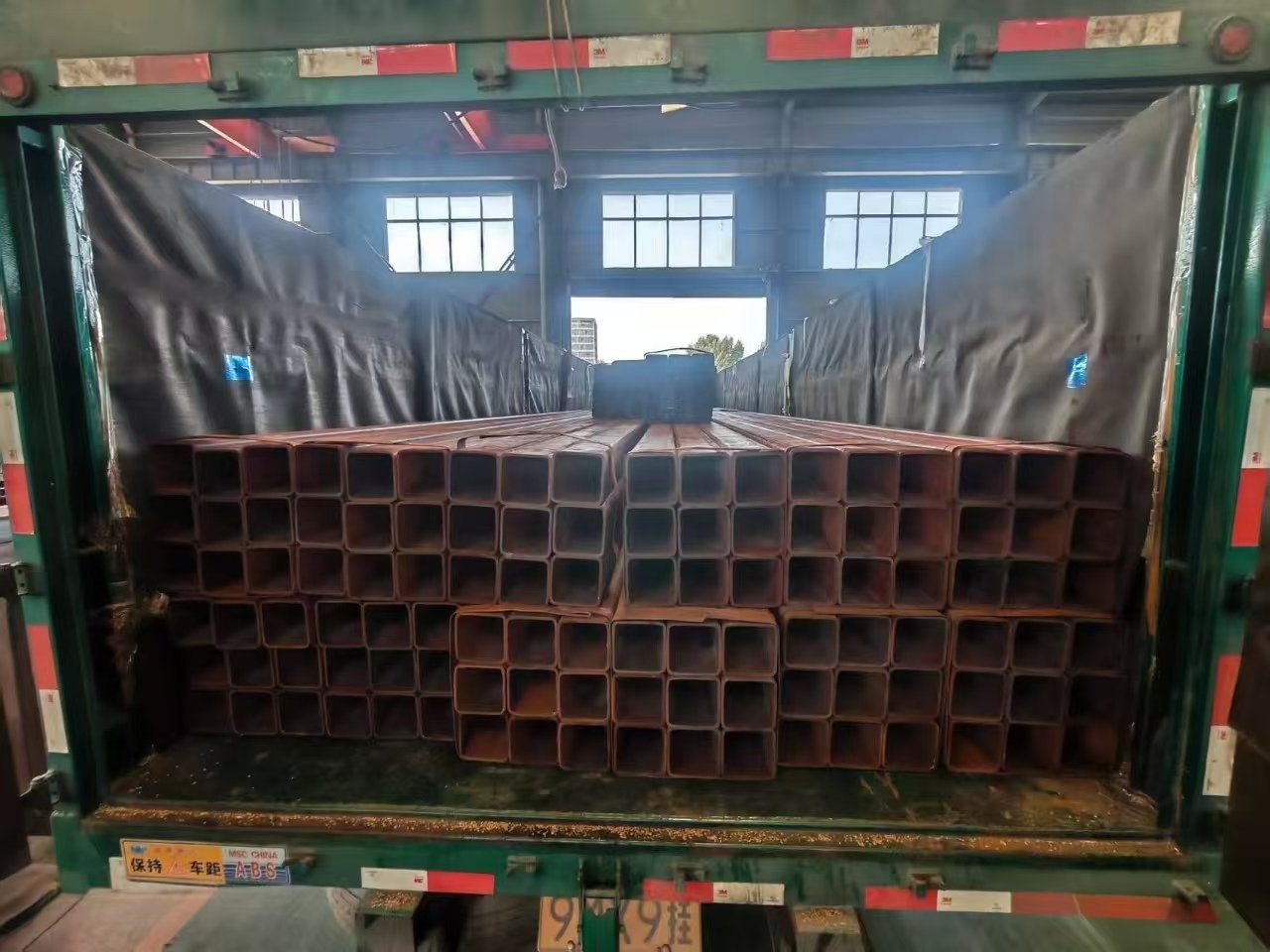 Crane handling bundled steel pipes during an outbound shipment.
